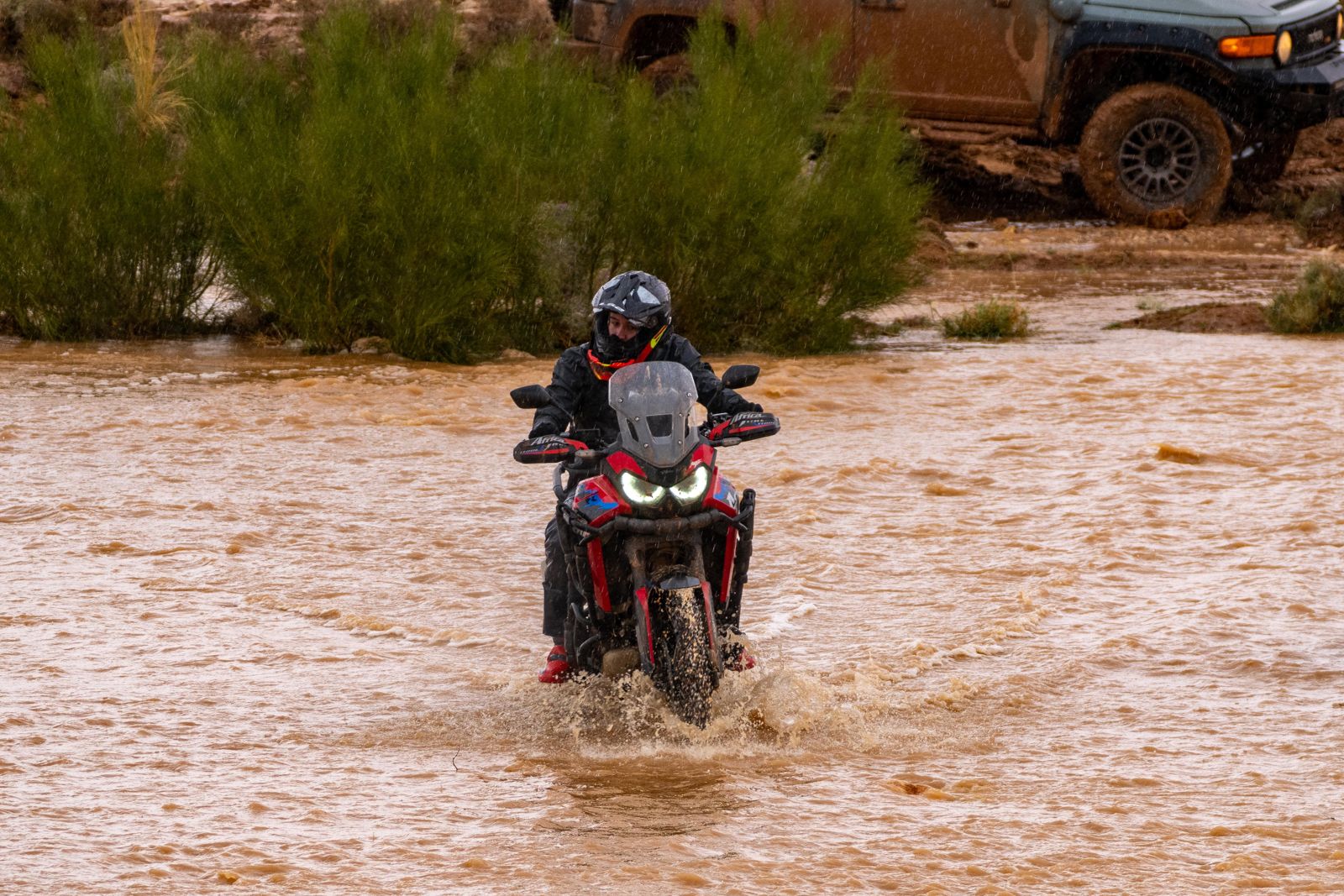 Piloto cruzando un río con el coche de asistencia detrás